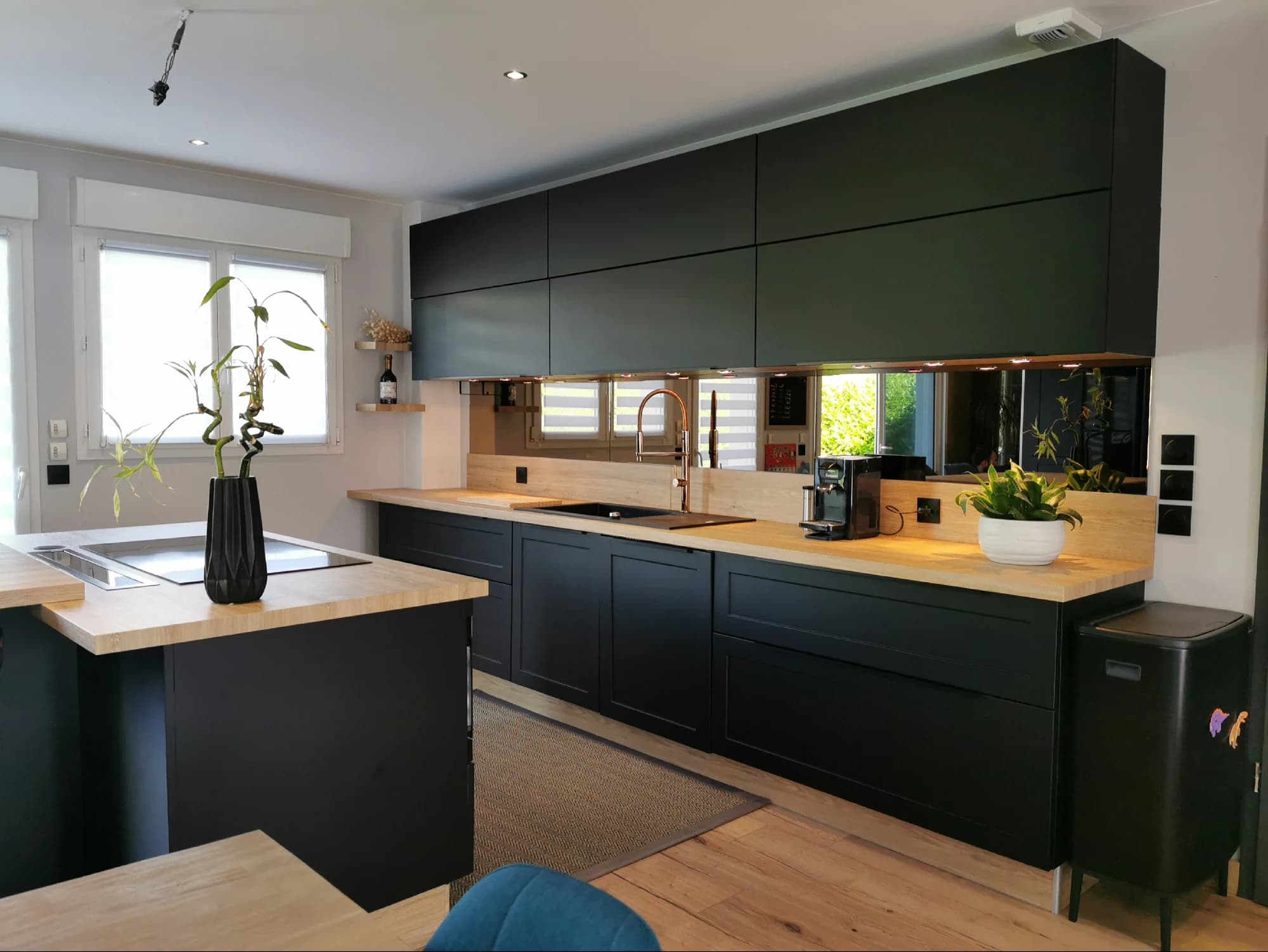 Cuisine relookée aux façades anthracite mates, plan de travail en bois et crédence miroir
