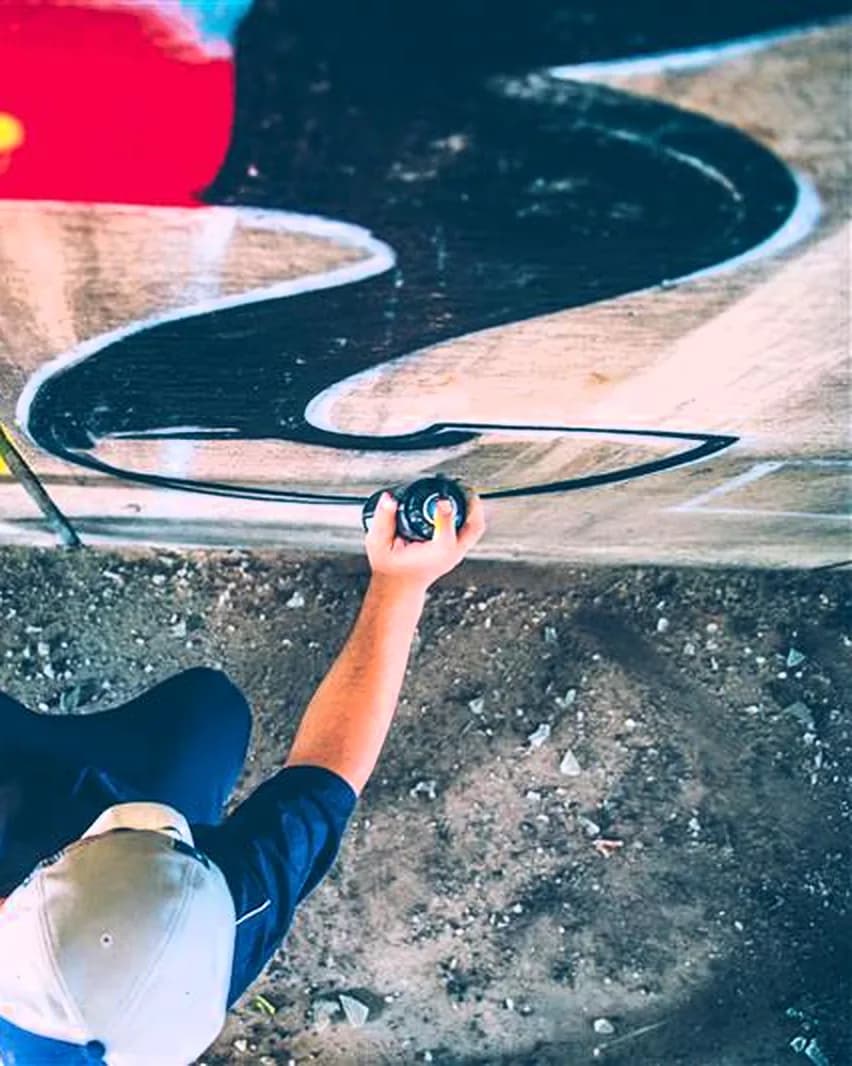 Graffeur vu de dessus, bombe de peinture à la main, devant un mur couvert de graffitis