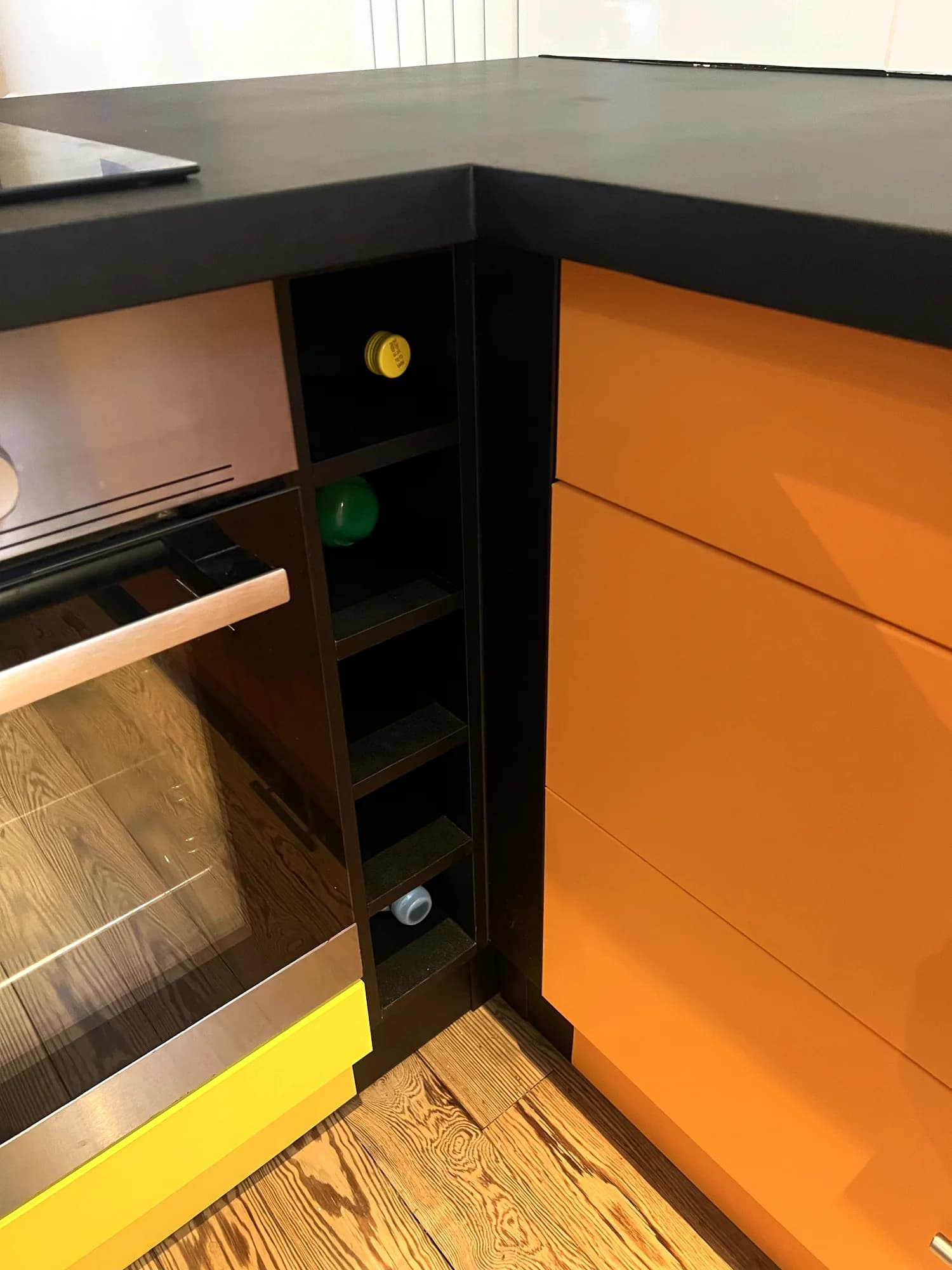 Plan de travail noir et façades orange autour d’un casier à bouteilles