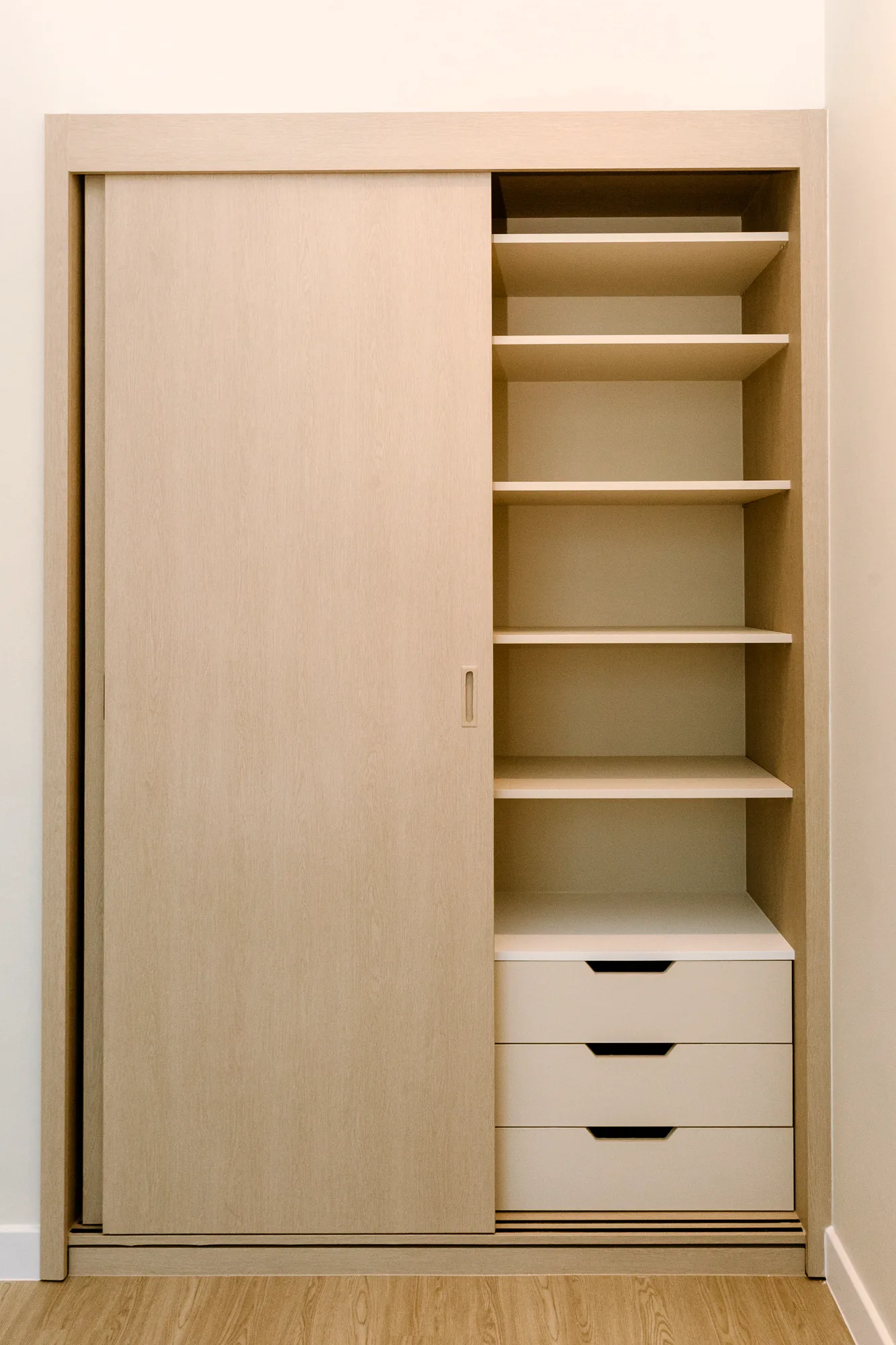 Dressing recouvert d’un vinyle bois clair, porte coulissante unie et tiroirs blancs